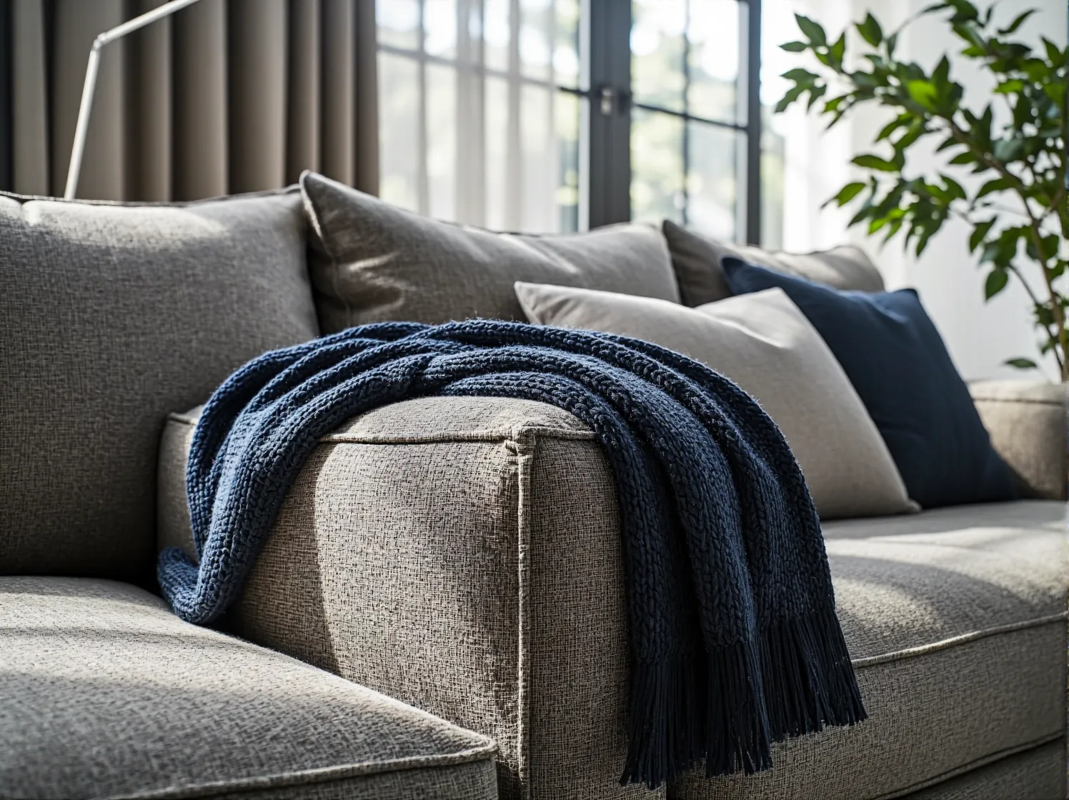 Szara sofa narożna ustawiona tyłem do panoramicznego okna w jasnym wnętrzu.